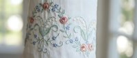 Delicate floral embroidery with pink roses and green vines on white fabric, showcasing traditional needlework craftsmanship for textile and home decor projects.