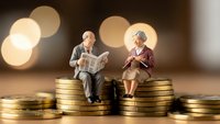 Senior couple miniature figures sitting on golden coin stacks representing retirement savings and financial planning for elderly lifestyle security.