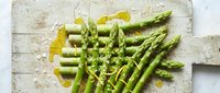 Fresh green asparagus spears with olive oil on rustic white wooden cutting board. Healthy organic vegetable ingredient for cooking and meal preparation.