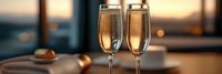 Two elegant champagne flutes filled with golden sparkling wine on wooden surface with warm bokeh lights creating romantic atmosphere for celebration.