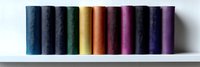 Colorful sewing thread spools arranged in rainbow spectrum order on white shelf, showing gradient transition from blue through yellow and pink to purple tones.