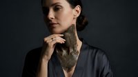 Young Caucasian woman in dark silk robe touching neck with large decorative leaf, studio portrait on dark background.