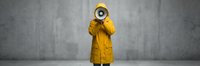Person in yellow raincoat holding megaphone against concrete wall background for communication and announcement concepts.