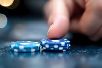 Blue casino poker chips with white dots on dark textured surface, finger pushing chip in blurred background, shallow depth of field creates dramatic gaming atmosphere.
