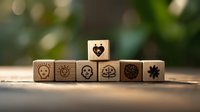 Wooden dice with creative icons including heart, skull, lightbulb, brain and flower symbols arranged in line on rustic surface against blurred natural background.