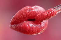 Sensual red lips with glitter sparkles and glossy finish in close-up macro shot against pink background, showing application of lipstick with applicator wand.