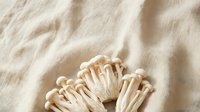 Enoki mushrooms with delicate white stems and caps arranged on natural linen fabric, suitable for food photography, culinary content, and organic ingredient styling.
