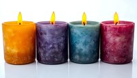 Colorful aromatic candles in orange, purple, teal and red arranged in row on white background with glowing flames and textured wax surface. For spa and home decor.