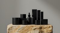 Black cosmetic packaging collection on natural stone platform for luxury skincare and beauty product branding.