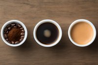 Three white cups on wooden background with coffee beans, ground coffee, black coffee, and creamy coffee showing preparation stages.