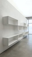 Modern minimalist white floating shelving system mounted on wall in contemporary interior space with concrete floors and natural light.