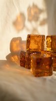 Amber glass ice cubes casting warm shadows on neutral surface with natural sunlight, suitable for beverage, luxury, and product photography.