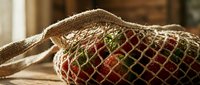 Eco-friendly mesh shopping bag filled with fresh organic vegetables and fruits on wooden surface for sustainable zero waste grocery shopping.