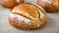 Freshly baked artisan sourdough bread with crispy crust and flour dusting on rustic wooden surface, perfect for gourmet food photography.