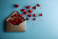 Red hearts flying out of opened kraft paper envelope on blue background, romantic love letter concept for Valentine's Day, wedding or anniversary celebration.