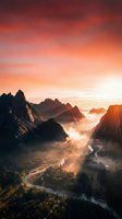 Dramatic mountain valley at sunrise with golden light illuminating jagged peaks, misty fog, and winding river below, perfect for travel and nature backgrounds.