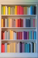 Colorful books arranged in rainbow order on white wooden shelves creating aesthetic gradient pattern. Modern minimalist library organization for interior design.