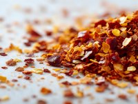 Red chili pepper flakes scattered on white surface with shallow depth of field for culinary and cooking applications.