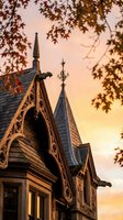 Victorian house architectural details with ornate gables and spires at golden hour sunset framed by autumn tree branches for home design projects.