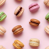 Colorful French macarons scattered on pink background, including pistachio, chocolate, vanilla and strawberry flavors creating sweet pattern composition.