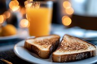 Fresh toasted bread slices on white plate with orange juice glass and bokeh lights in background, morning breakfast setting with warm lighting.