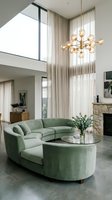 Modern living room with curved sage green sectional sofa, round glass coffee table, brass globe pendant lighting, floor-to-ceiling sheer curtains, stone fireplace, and high ceilings with skylights.
