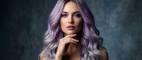Young woman with purple silver hair and dramatic makeup posing elegantly against dark textured background for beauty and fashion concepts.