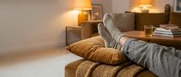 Person relaxing at home with feet up on cozy sofa in warm living room with soft lighting and moving boxes in background for relocation concept.