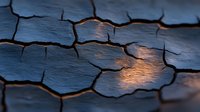 Dramatic cracked dry earth texture with warm sunset light creating contrast between deep crevices and illuminated surfaces, natural abstract pattern in blue and orange tones.