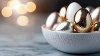 Metallic gold and silver Easter eggs in white ceramic bowl with soft bokeh lights background, modern minimal holiday decoration on marble surface.