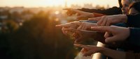 Group of diverse hands reaching together in golden sunset light symbolizing unity teamwork collaboration and community support outdoors.