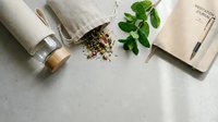 Natural herbal tea ingredients with fresh mint leaves, dried herbs, linen napkins and notebook on marble surface for wellness lifestyle branding.