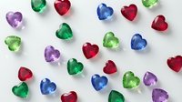 Colorful heart-shaped gemstones scattered on white background. Precious stones in red, blue, green, purple hues for jewelry design and romantic themes.