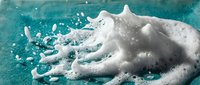 Hands covered in white foam soap bubbles against turquoise background for hygiene and cleanliness concepts in healthcare and personal care applications.