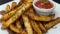 Crispy seasoned potato wedges with fresh herbs and spicy ketchup dipping sauce on white plate, close up view of golden brown fried potatoes.