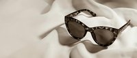 Stylish tortoiseshell cat-eye sunglasses with dark lenses resting on soft white fabric creating elegant shadows for fashion and eyewear accessories.