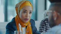 Young Middle Eastern businesswoman wearing yellow hijab and navy blazer listening intently during office meeting, displaying professional engagement and focused attention.