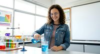 Young Hispanic female chemistry teacher conducting science experiment with blue liquid in modern classroom laboratory setting for educational demonstration.