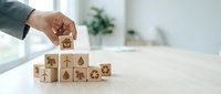 Businessman hand arranging wooden cubes with environmental sustainability icons including recycling, renewable energy, and eco-friendly symbols on office desk.