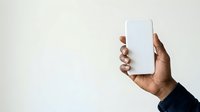Man with dark skin tone holding blank white smartphone against neutral background, suitable for app mockups, technology marketing, mobile device advertising, and digital product presentations.