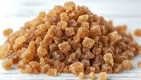 Brown sugar crystals macro shot on white wooden background, showing natural organic sweetener texture and crystalline structure. Food ingredient closeup.