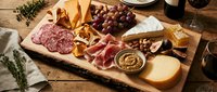 Gourmet charcuterie board with assorted meats, cheeses, grapes, nuts and crackers on wooden serving platter for entertaining and wine pairing.
