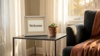 Cozy living room corner with a welcome sign in a frame, small succulent plant, and armchair with blanket by a sunny window.