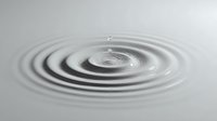 Concentric ripples forming on calm water surface after droplet impact, creating peaceful circular waves against minimalist gray background.