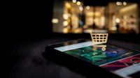 Mobile shopping cart icon on smartphone screen with blurred retail store background showcasing modern e-commerce and online shopping technology.