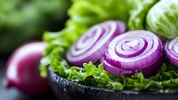 Fresh sliced red onion rings garnished with green lettuce leaves on dark plate, macro food photography with selective focus and vibrant colors.