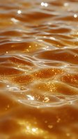 Shimmering golden liquid surface with sparkling particles and gentle waves creating a luxurious caramel-colored background texture for food and beverage designs.