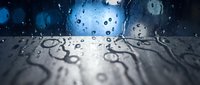 Water droplets on glass surface with blurred blue background creating abstract wet texture for modern design and atmospheric mood concepts.