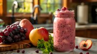 Fresh fruit smoothie in mason jar with raspberries, peach, grapes and mint on wooden board. Pink healthy breakfast drink garnished with berries and chia seeds.