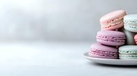 Pastel pink and mint macarons arranged on white ceramic plate against light background, soft focus food photography for bakery marketing and social media.